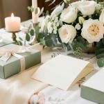 Coffrets cadeaux élégants et cartes vierges soigneusement disposés sur une table de réception décorée de fleurs blanches et d’eucalyptus.