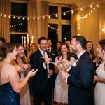 Des invités élégamment habillés s’amusent après minuit lors d’une réception de mariage avec des jeux silencieux, des lumières chaleureuses et une ambiance festive.
